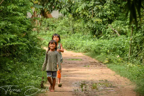 Two young girls walk along a jungle path towards the camera